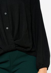 Black lightweight blouse featuring a relaxed fit, button closure, and long sleeves with gathered cuffs, paired with dark green pants.