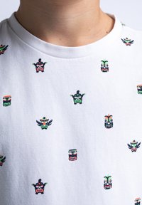 Bílá bavlněná tričko s vzorem malých, barevných kmenových masek v zelené, červené a černé barvě, s kulatým výstřihem.