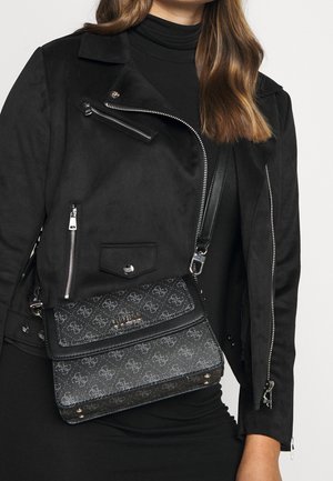 Black leather crossbody bag with embossed logo pattern, flap closure, and silver hardware accents, worn over a fitted black dress.