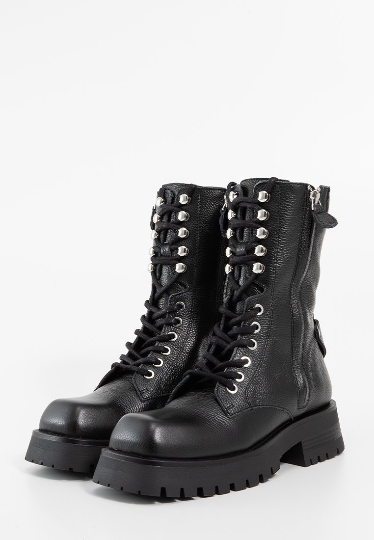 Bottines noires en cuir avec une texture mate, dotées d'œillets en métal argenté, d'un laçage à l'avant et d'une semelle en caoutchouc épaisse et rainurée.