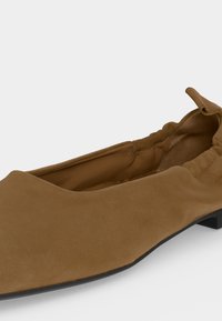 Chaussure plate en daim marron avec un bout arrondi, un col élastique froncé et un petit talon noir.