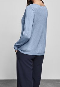 Vaaleansininen neule pehmeästä materiaalista, jossa on pitkät hihat, pyöreä pääntie ja rento istuvuus. Yhdistetty tummansinisiin housuihin.