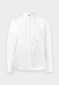 Chemise blanche à manches longues boutonnée avec col officier, plastron texturé et petit logo brodé "AX" sur le côté droit.