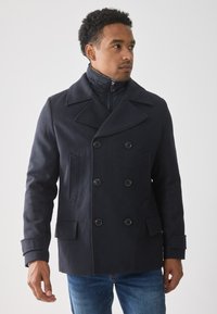 Abrigo marino de doble botonadura con grandes solapas, cuello con cremallera y dos bolsillos laterales; textura de lana suave, con botones negros.