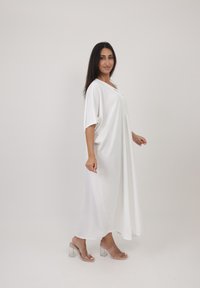 Robe blanche ample avec des manches courtes, décolleté en V et un design fluide. Portée avec des sandales à talons transparents. Texture de tissu lisse.