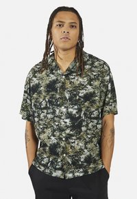 Korte mouwen shirt in zwart en groen met een botanisch print. Knopen aan de voorkant, kraag en een relaxte pasvorm. Gemaakt van lichtgewicht stof.