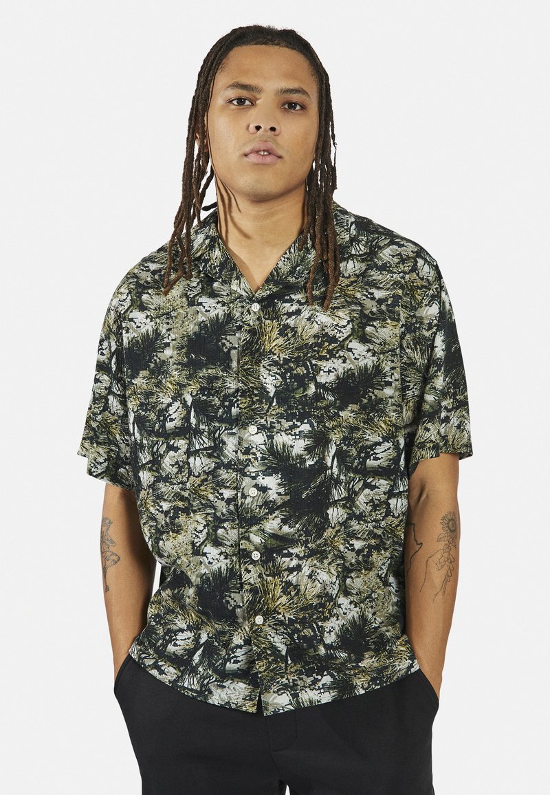 Korte mouwen shirt in zwart en groen met een botanisch print. Knopen aan de voorkant, kraag en een relaxte pasvorm. Gemaakt van lichtgewicht stof.