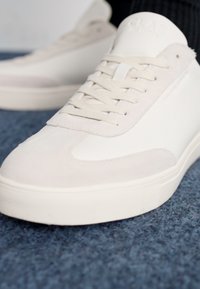 Sneaker bianco realizzato in pelle e scamosciato, con lacci piatti, punta tonda e suola in gomma testurizzata. Design minimalista con un morbido contrasto di colore.