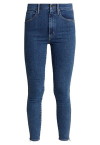 Tmavě modré džíny úzkého střihu z denimu, s vysokým pasem, předními kapsami a jemným opotřebovaným vzhledem u lemu.