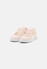 Puma suede tenisice u mekom ružičastoj boji s bijelim gumeni potplatima. Imaju šivaju tonovima i zlatni logo na jeziku i bočnoj strani.