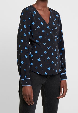 Czarna bluzka kopertowa z niebieskim kwiatowym wzorem i długimi rękawami, noszona z czarnymi dżinsami, pokazana od połowy tułowia do szyi i rąk.