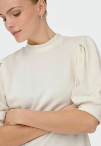 Sweater in soft white fabric, featuring a high neckline and puffed short sleeves with ribbed cuffs. Smooth texture with slight sheen.