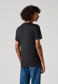 Svart t-skjorte med kort erm og rund hals, vist bakfra. Kombinert med blå denimjeans. Myk bomullsmateriale med en glatt tekstur.