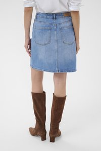 Denim krilo v svetlo modri barvi z ravnim krojem, dvema zadnjima žepoma in surovim robom; v kombinaciji z rjavimi semiš škornji do kolen.
