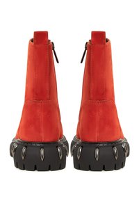 Bottes chevilles en daim rouge avec semelles épaisses noires ornées de détails métalliques en forme de pointes, vues de dos.