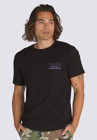 Camiseta de algodón negra con mangas cortas, que presenta un logo morado de Vans en el área del pecho izquierdo. La tela tiene una textura suave.