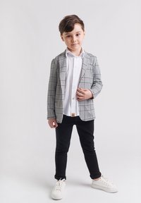 Marynarka w kratę w czerni i bieli, biała koszula, czarne spodnie i białe trampki. Marynarka ma klapy typu notch i dwie przednie kieszenie.