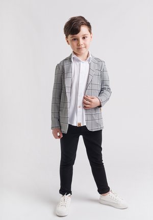 Marynarka w kratę w czerni i bieli, biała koszula, czarne spodnie i białe trampki. Marynarka ma klapy typu notch i dwie przednie kieszenie.