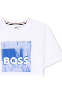 Balta kokvilnas T-kreklu ar zilu grafikā kvadrātu, kurā ir „BOSS” teksts treknā baltā fontā. Apļveida kakla izgriezums un īsas piedurknes.