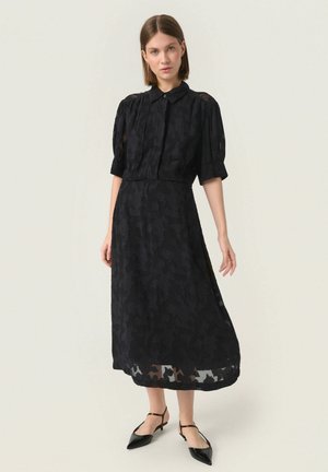 Schwarzes Midikleid mit Kragen und Puffärmeln; aus strukturiertem Stoff mit einem floralen Muster und einem halbtransparenten Saum.