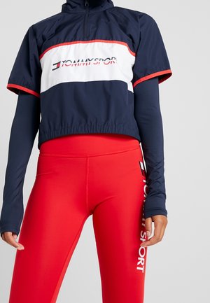 Laivastonsininen ja valkoinen lyhyt urheilutakki punaisilla reunuksilla ja siihen sopivat punaiset korkeavyötäröiset leggingsit, molemmissa Tommy Sport -logot.