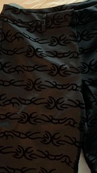 Black fabric featuring a textured pattern of flowing, abstract designs. Smooth surface with a slight sheen. Secure waistband at the top.