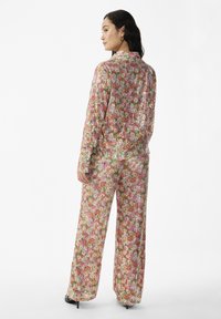 Floral patterned two-piece outfit featuring a long-sleeve shirt and wide-leg pants in pink, green, and gold hues with a shiny texture.