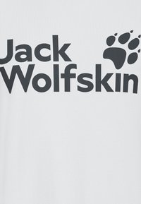 T-shirt blanc avec un texte noir audacieux indiquant "Jack Wolfskin" et un motif d'empreinte de patte noire, en coton doux.