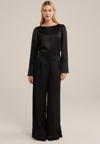 Top in raso nero con maniche lunghe e scollatura rotonda, abbinato a pantaloni neri a vita alta e gamba larga con pieghe.