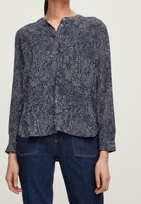 Donna che indossa una blusa a maniche lunghe blu navy a motivo con scollatura rotonda abbottonata a metà, abbinata a jeans blu scuro.
