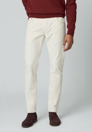 Jeans en denim blanc avec poches avant, forme ajustée et léger stretch. Associés à des bottes en daim marron et un pull en tricot bordeaux.