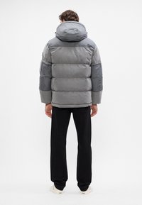 Chaqueta de plumas gris con una gran capucha, con un diseño acolchado y puños elásticos, combinada con pantalones negros y zapatos en tonos neutros.