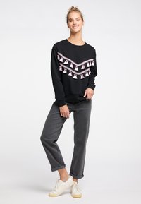 Hanorac negru cu trim de ciucuri roz, mâneci lungi, guler circular; asortat cu blugi gri cu tiv și adidași albi. Design simplu, casual.