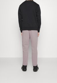 Sudadera negra con cuello redondo, combinada con pantalones de chándal morados claros. El conjunto presenta puños elásticos y una textura de tela suave. Zapatillas negras.