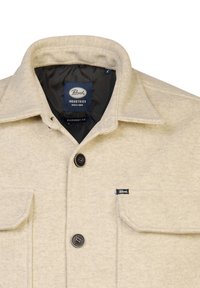 Beige overshirt made of textured fabric, featuring a point collar, two front pockets, and black button closures. Label inside reads "Petrol Industries."