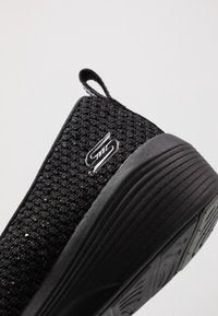 Černá nazouvací bota s texturovaným síťovaným svrškem a podpisovým logem. Obsahuje gumovou podešev s členitým vzorem pro lepší trakci.