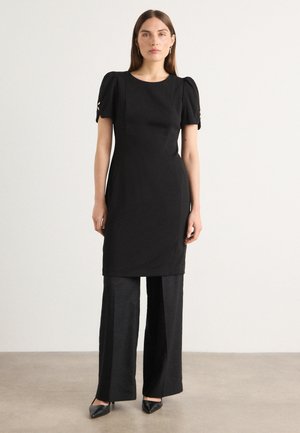 Black dress with puff sleeves, a round neckline, and gold accents at the sleeve cuffs, paired with wide-leg black trousers and pointed shoes.