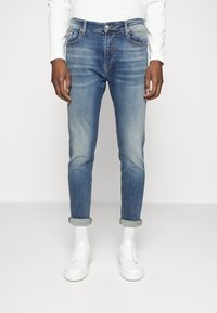 Ljusblå denimjeans med slim fit, som har framfickor, kontrasterande sömmar och uppvikta fållar, tillsammans med vita sneakers och strumpor.