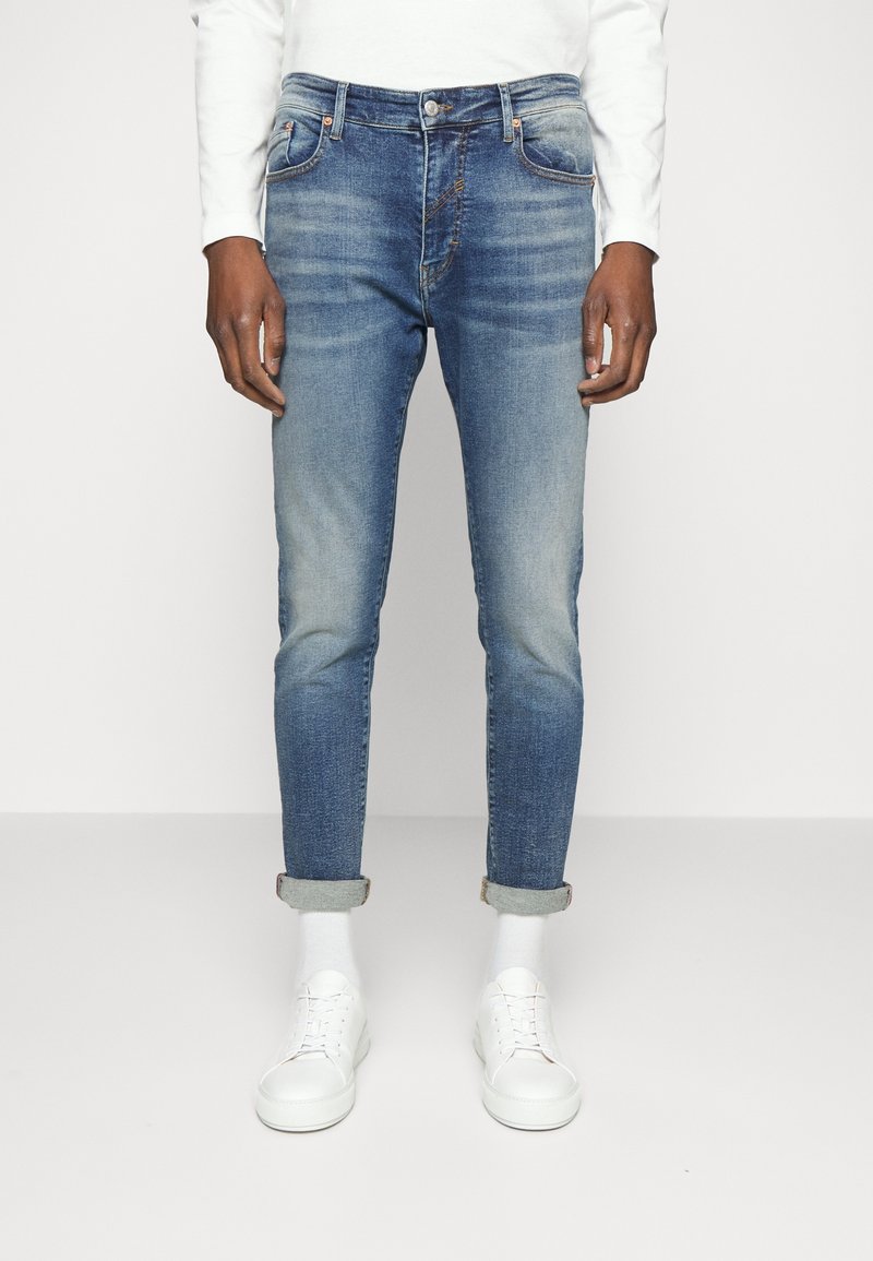 Ljusblå denimjeans med slim fit, som har framfickor, kontrasterande sömmar och uppvikta fållar, tillsammans med vita sneakers och strumpor.