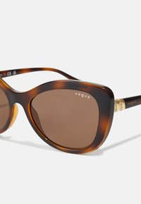Ochelari de soare cu nuanță de maro, cu rame din plastic cu model țestoasă, formă supradimensionată, accente aurii pe mânere și brandul "vogue" în argintiu.