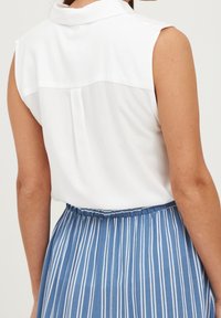 Vit ärmlös blus med krage och ryggholk, i kombination med en blå och vit randig kjol med vertikala ränder och resårmidja.