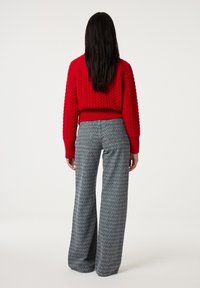 Rode gebreide korte trui met gestructureerde kabels en een geribbelde zoom, gecombineerd met hoge, grijze broekspijpen met een subtiel patroon.