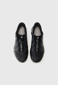 Black athletic shoes featuring a textured surface, mesh elements, and a secure lacing system with reflective accents on the heel.