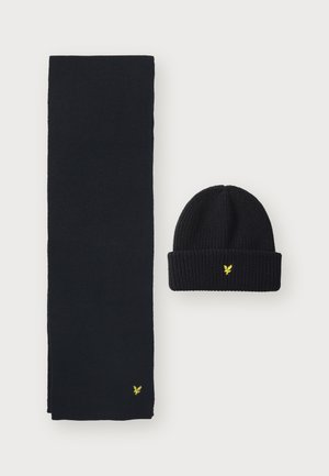 Bufanda de punto negra y gorro, ambos con un sutil logo amarillo. La bufanda es larga y rectangular, mientras que el gorro es acanalado con un borde doblado.