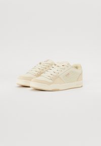 Beige sneakers met een mix van suede en leer, voorzien van een textuurpaneel aan de zijkant, roze accenten en platte veters. Laag profiel rubberen zool.
