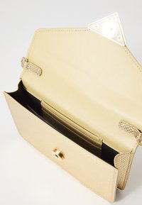 Borsa a mano color oro, con esterno testurizzato, interno liscio, scomparti per carte e chiusura magnetica con un accento circolare.