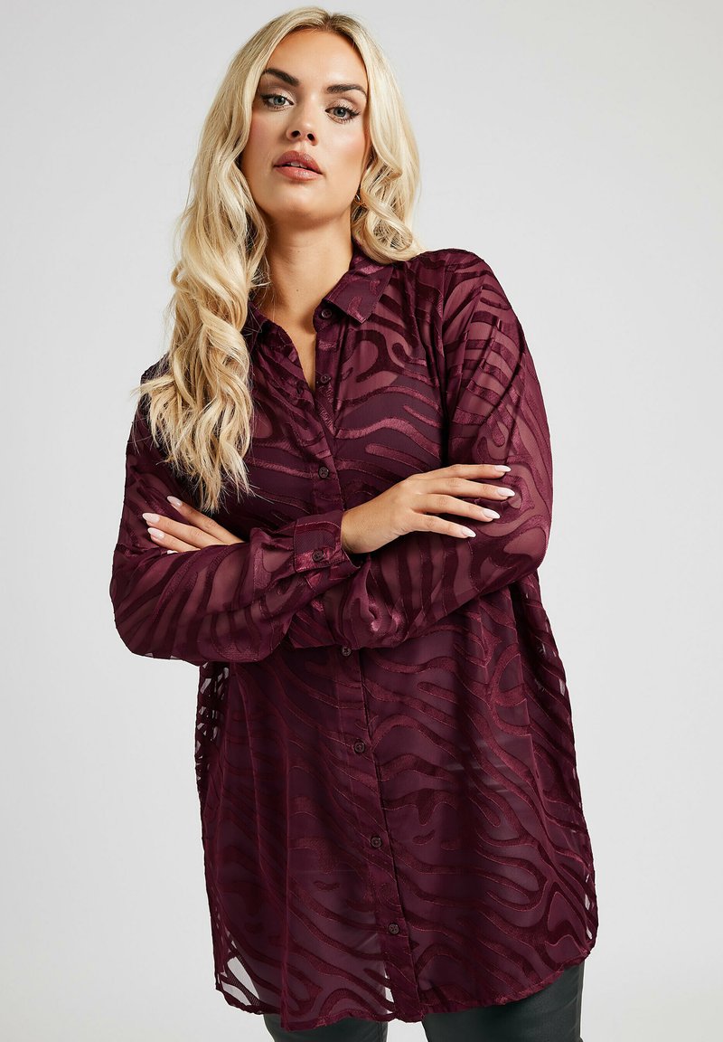 Burgundy genomsiktlig skjorta med knappar, med en texturerad zebramönster, långa ärmar och en avslappnad passform, som visar en lätt, flödande tyg.
