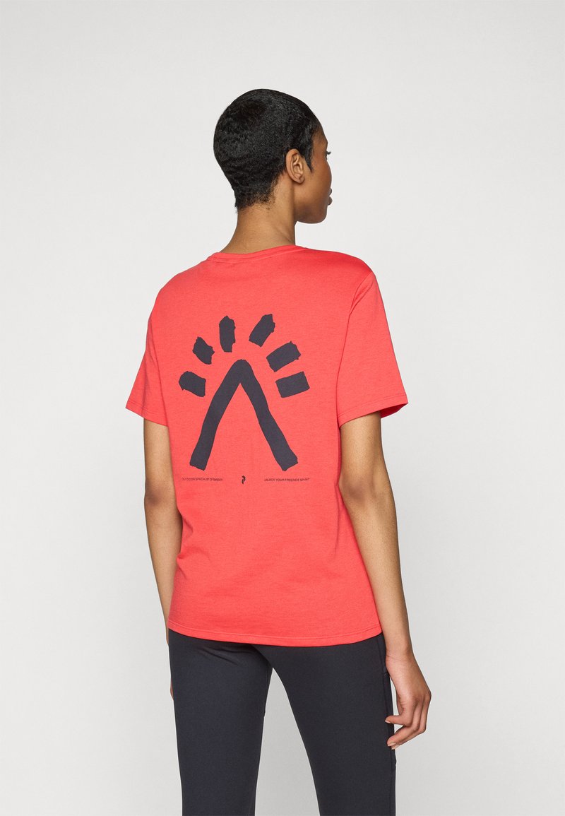 Red t-shirt with a short sleeve and a large black graphic design on the back, featuring an arch and rays. Fabric appears soft and smooth.