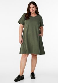 Short-sleeve, A-line dress in olive green, made of soft fabric with side pockets and a round neckline, paired with black platform loafers.