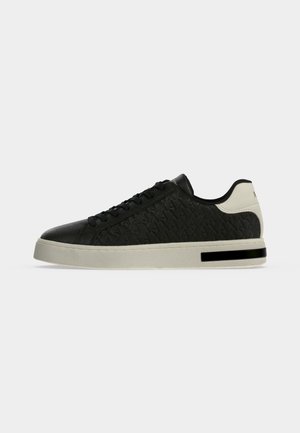 Low-top black sneaker with embossed pattern, black laces, white heel section, and white sole with a black rectangular detail.